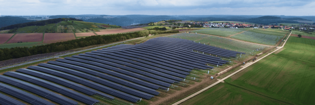 Solarpark Uissigheim auf h&uuml;geligen Feldern mit einem Dorf im Hintergrund.